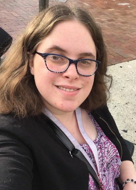Color photo of Cara Liebowitz, a youthful white woman with shoulder-length brown hair and glasses, who is smiling.