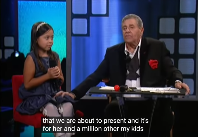 Telethon screenshot. Lewis has his hand grabbing a young girl's knee. "that we are about to present and it's for her and a million other of my kids"